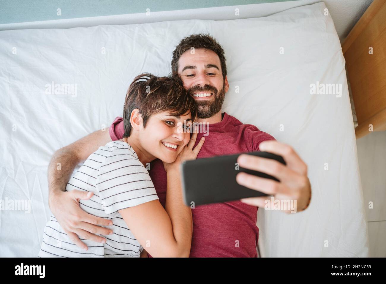 Man with woman taking selfie though smart phone while lying on bed Stock Photo