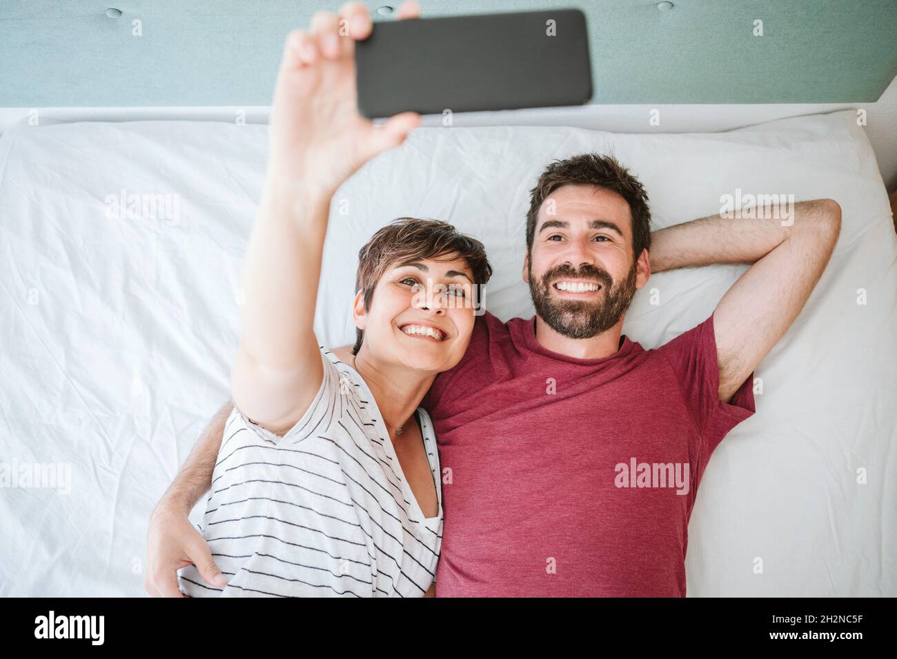 Woman taking selfie with man through smart phone while lying on bed at home Stock Photo