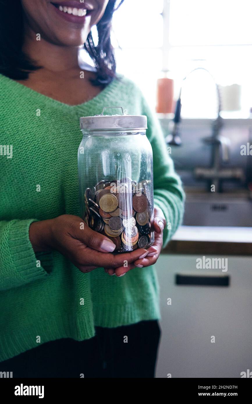 Smiling woman holding coin's jar at home Stock Photo