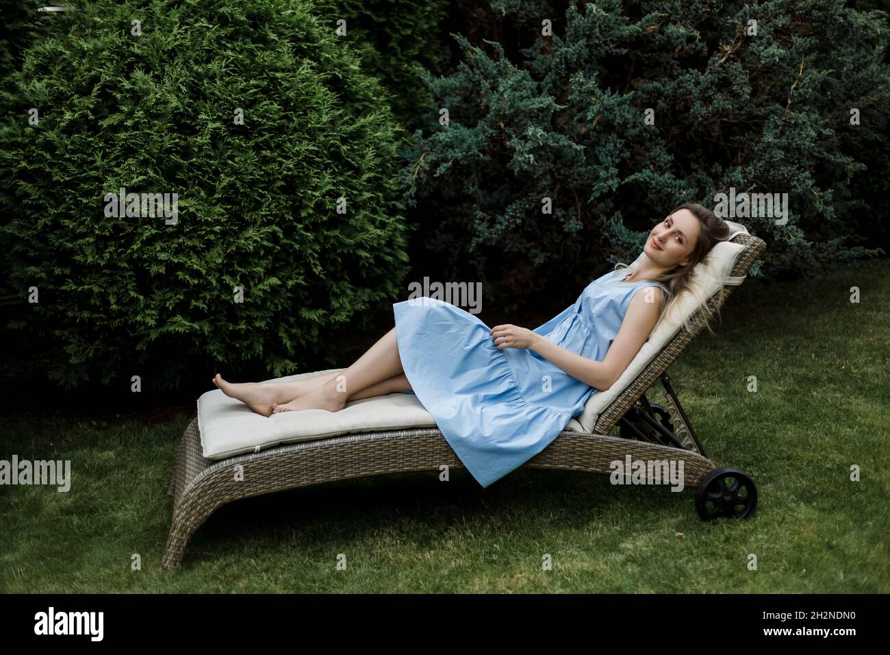 Woman relaxing on deck chair by plants in garden Stock Photo - Alamy