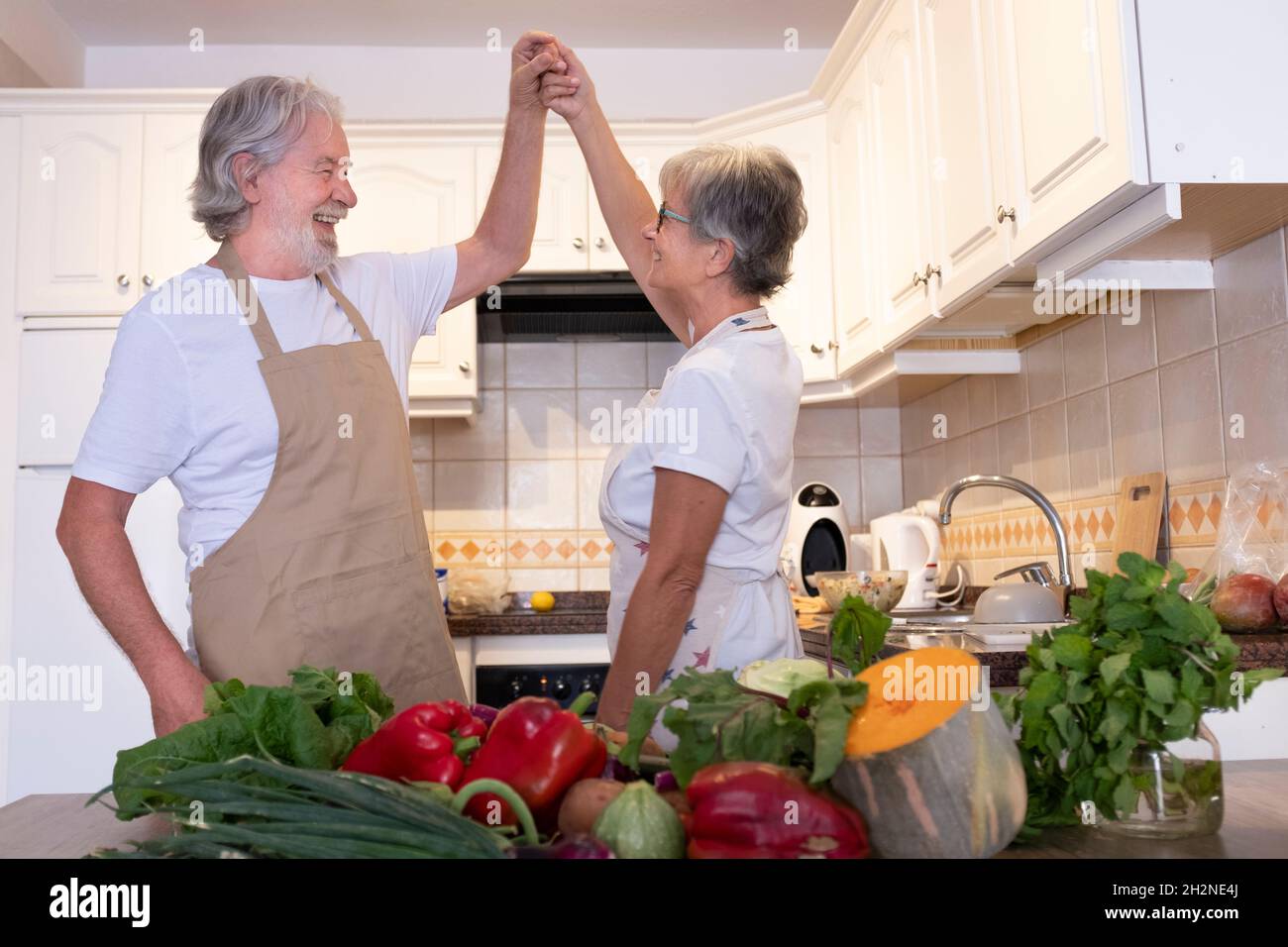 Senior couple holding hands while dancing in kitchen Stock Photo