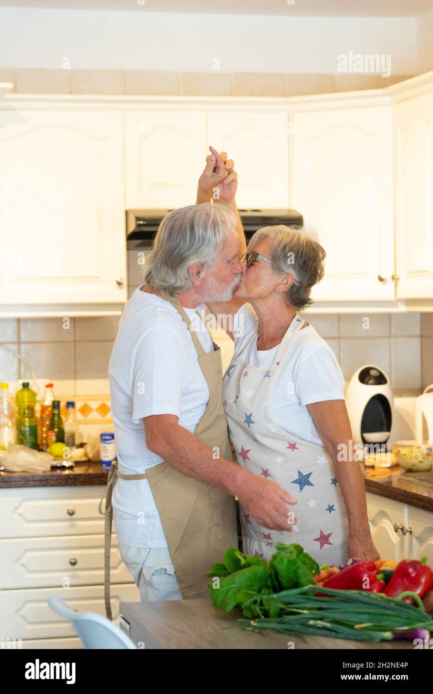 Senior couple holding hands while kissing in kitchen Stock Photo