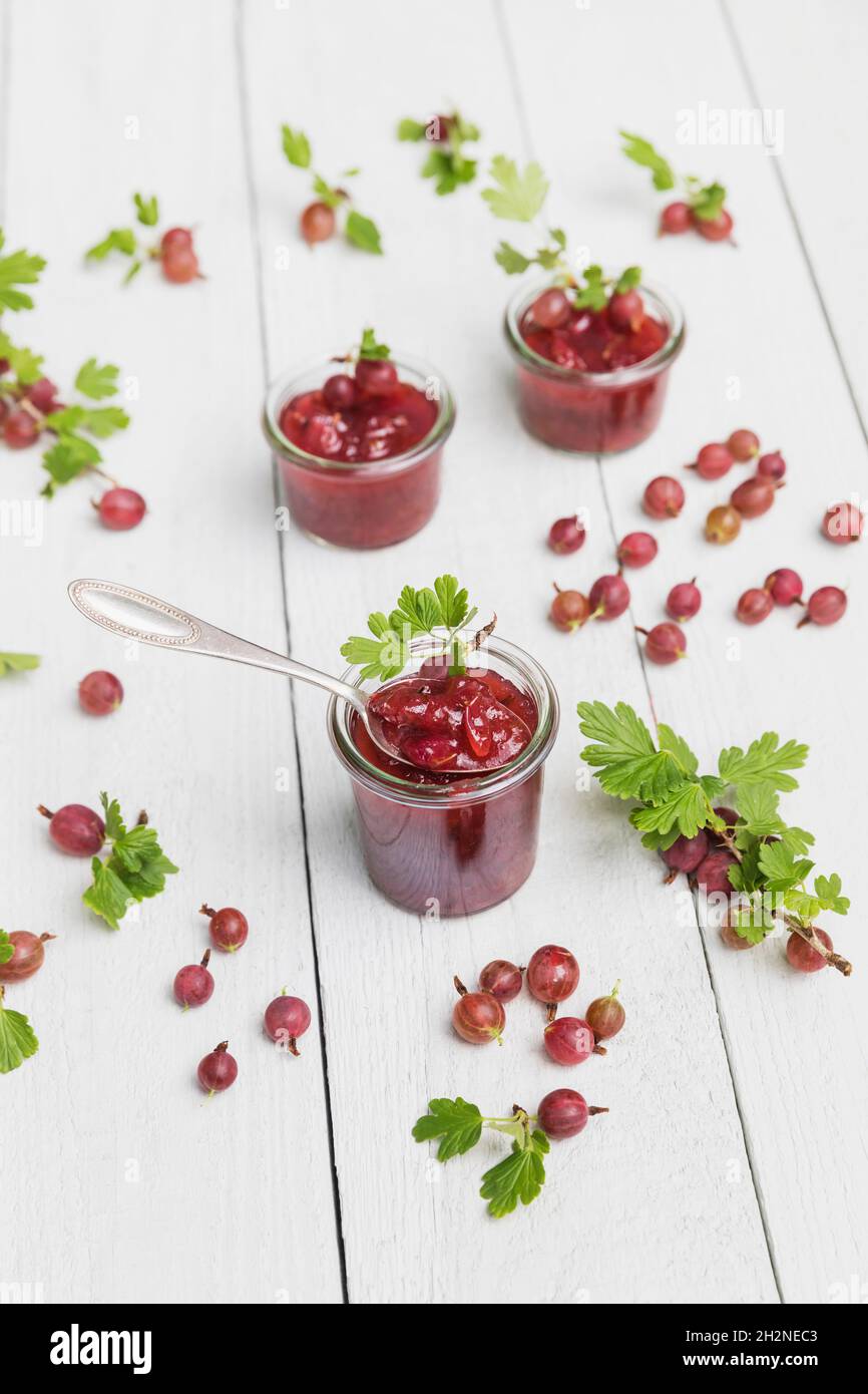 Raw gooseberries (Ribes uva-crispa) and jars of homemade gooseberry jam lying on white table Stock Photo