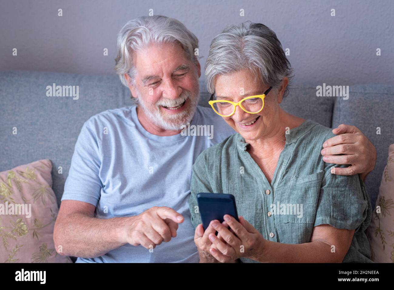 Smiling bearded man pointing at mobile phone while sitting by woman in living room Stock Photo