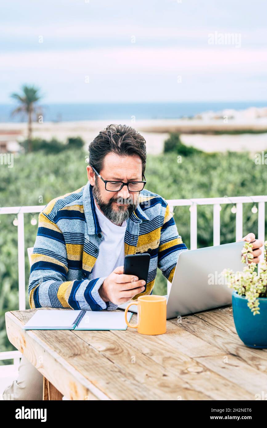 Bearded man with laptop using mobile phone at table Stock Photo