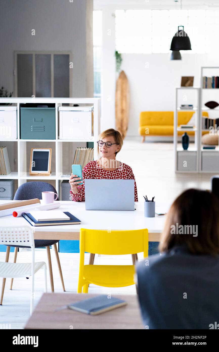 Businesswoman with laptop looking at female colleague in office Stock Photo