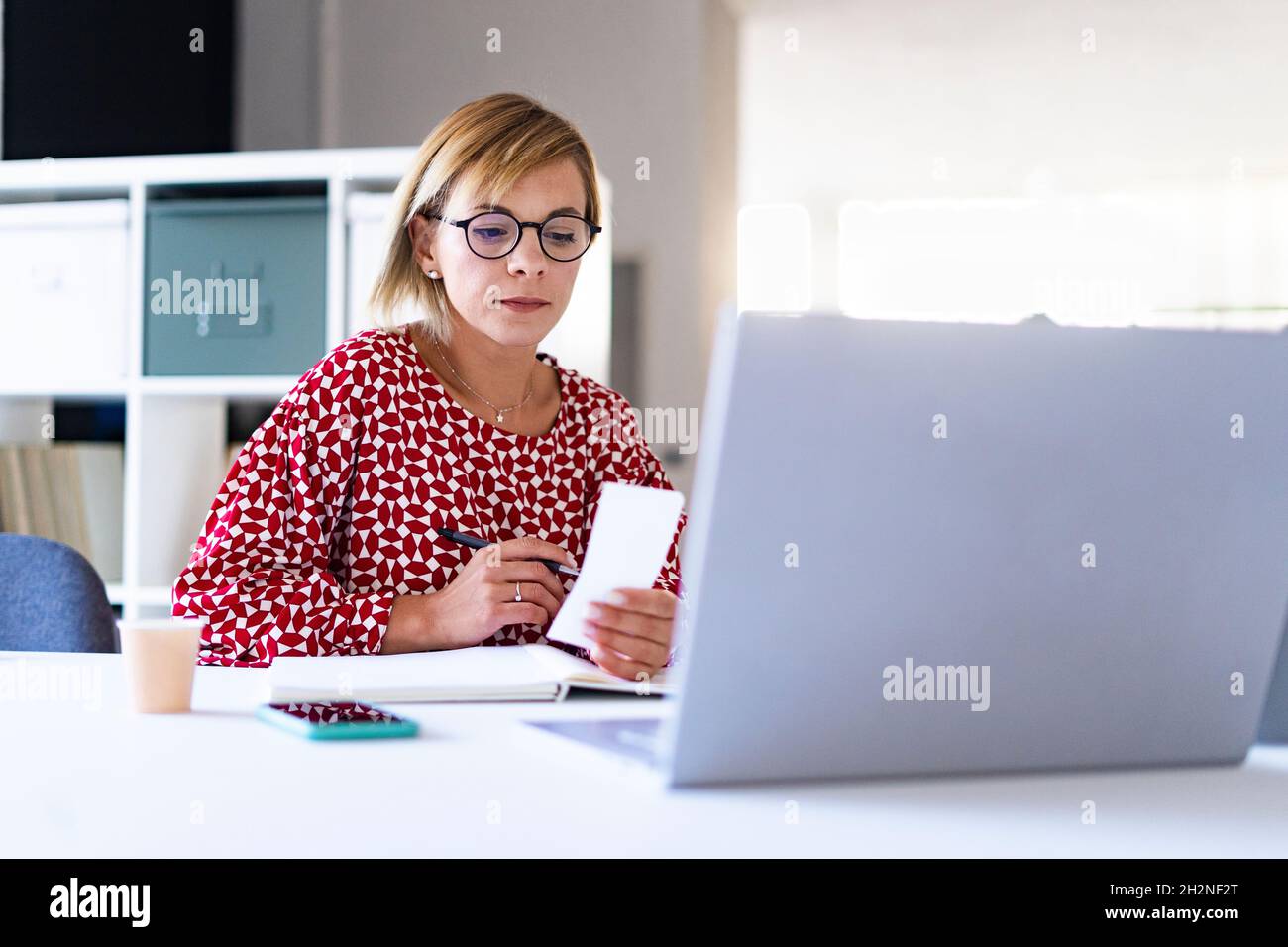 Thoughtful female professional looking at laptop in office Stock Photo