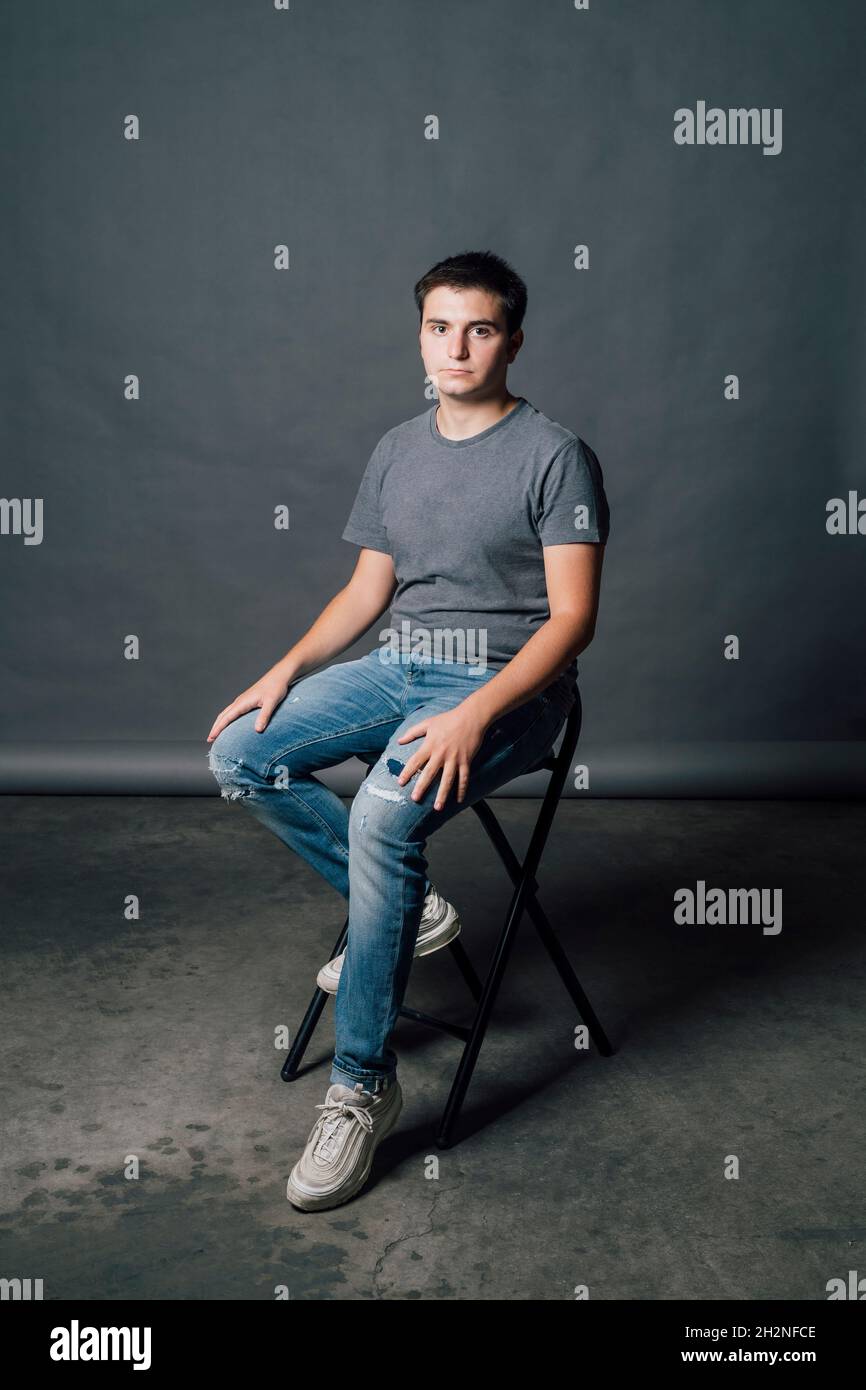 Young man sitting on chair by gray backdrop in studio Stock Photo - Alamy