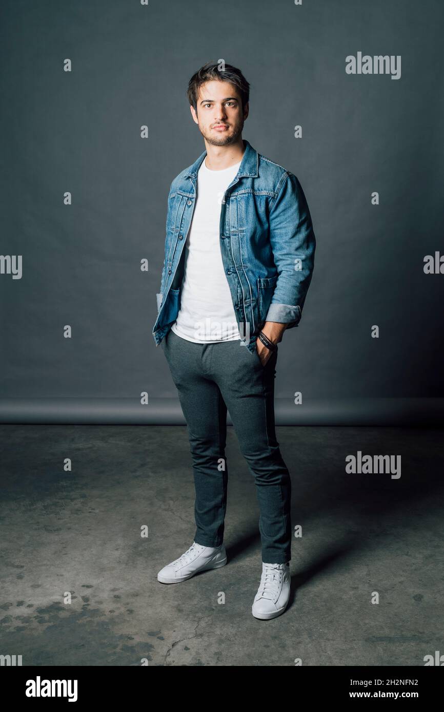 Young man wearing denim jacket while standing with hands in pockets Stock Photo