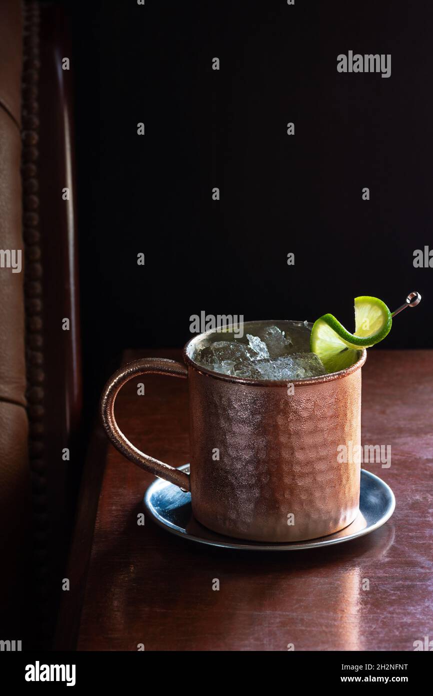 Moscow Mule Cocktail Drink with Crushed Ice and Lime in Copper Mug in Dark Luxurious Bar Stock Photo