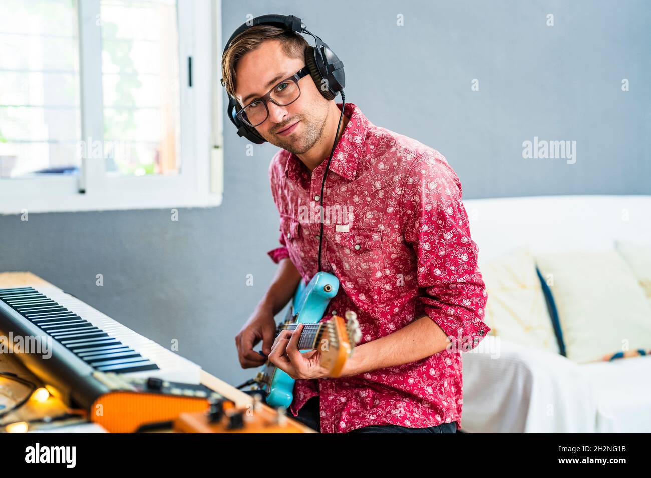 Male guitarist with headphones playing guitar at home Stock Photo