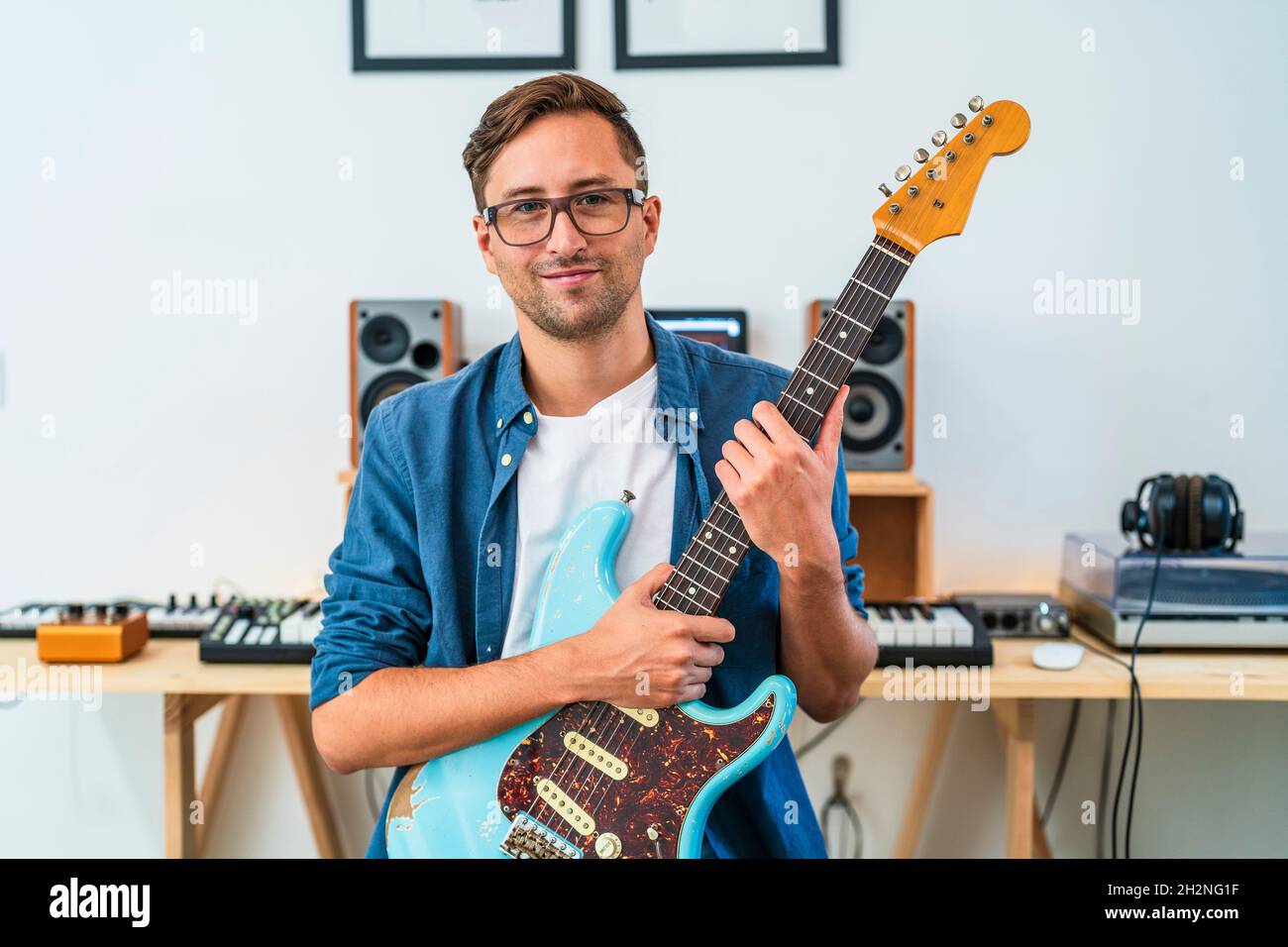Male guitarist wearing eyeglasses holding guitar at home Stock Photo