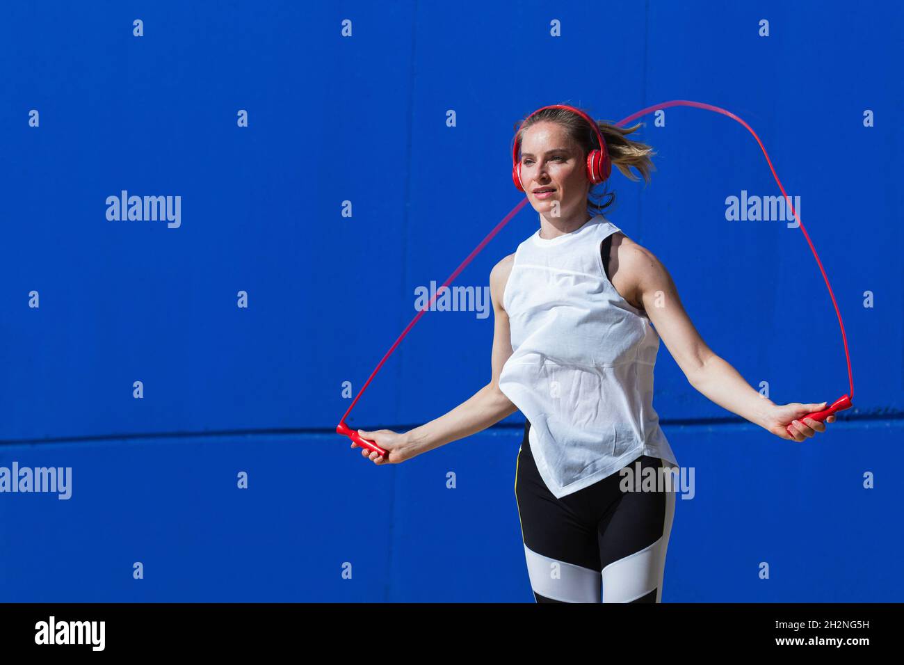Female athlete jumping rope in front of blue wall Stock Photo - Alamy
