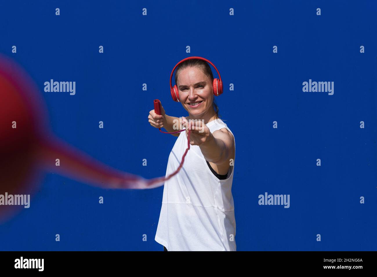 Smiling female athlete holding jump rope in front of blue wall Stock ...