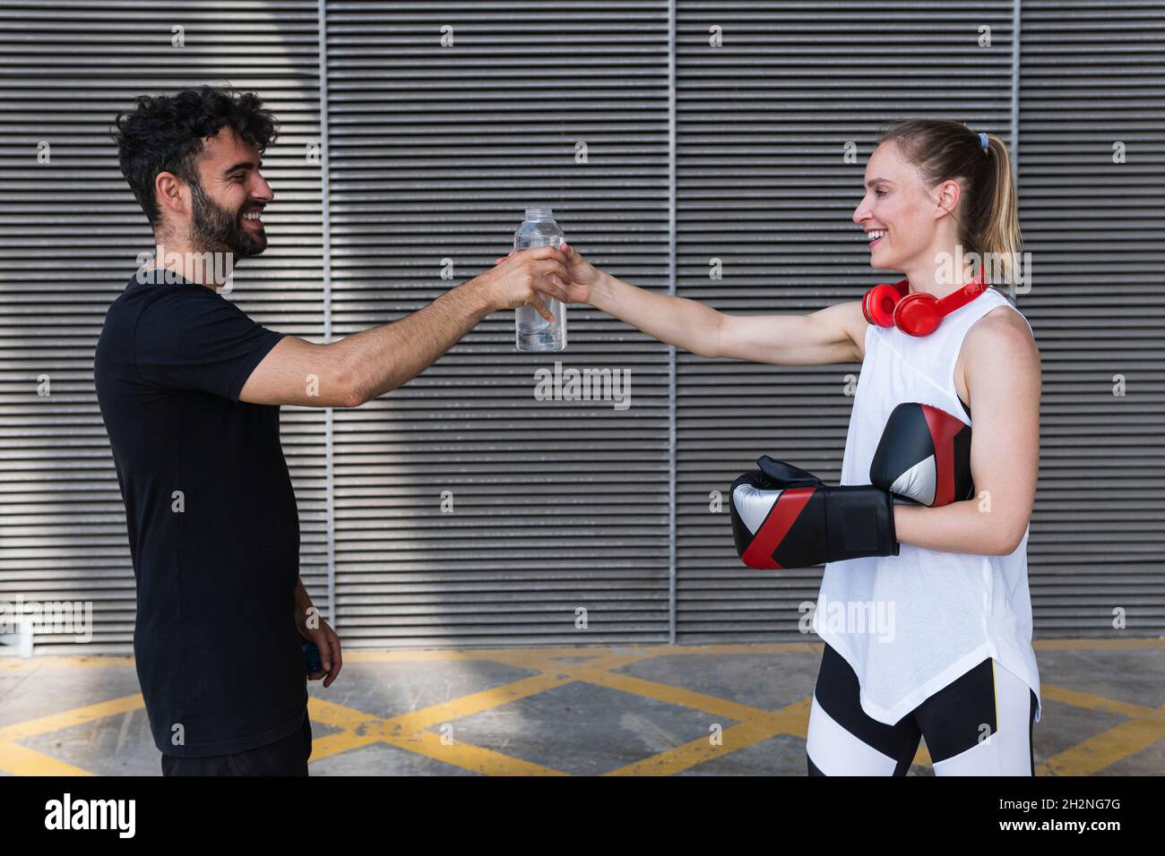 Smiling female boxer sharing water with male coach in front of wall ...