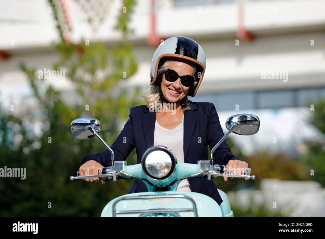 Pretty woman in white costume and sunglasses sitting on moped happily  taking selfie in city center Stock Photo by garetsworkshop