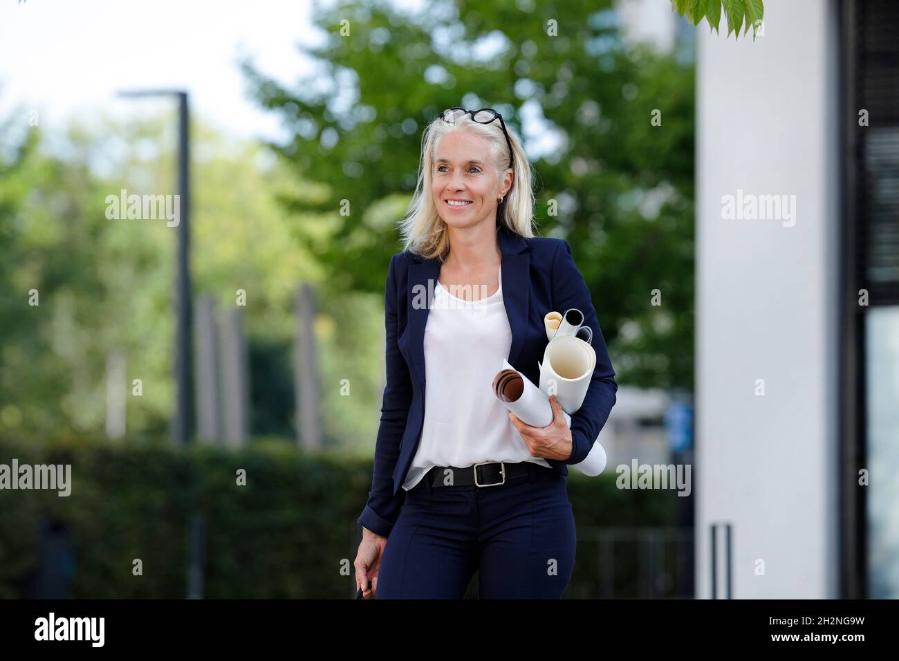 Mature businesswoman looking away while carrying blueprints Stock Photo