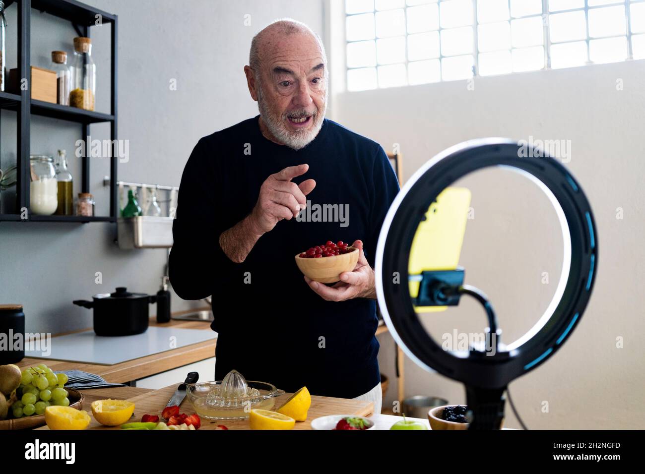 Male influencer with lemon filming through mobile phone at kitchen counter Stock Photo