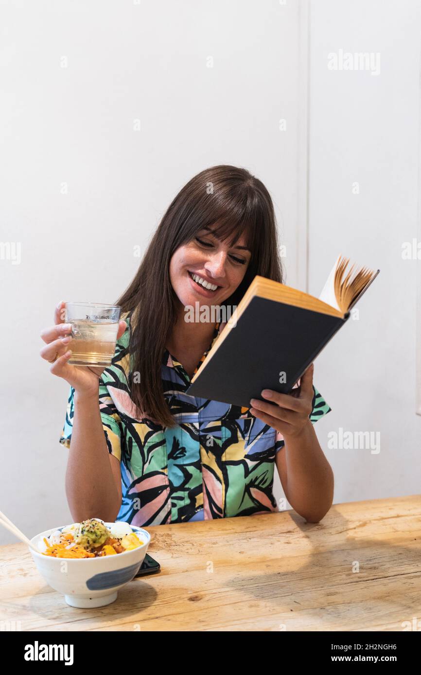Smiling woman reading book in restaurant Stock Photo