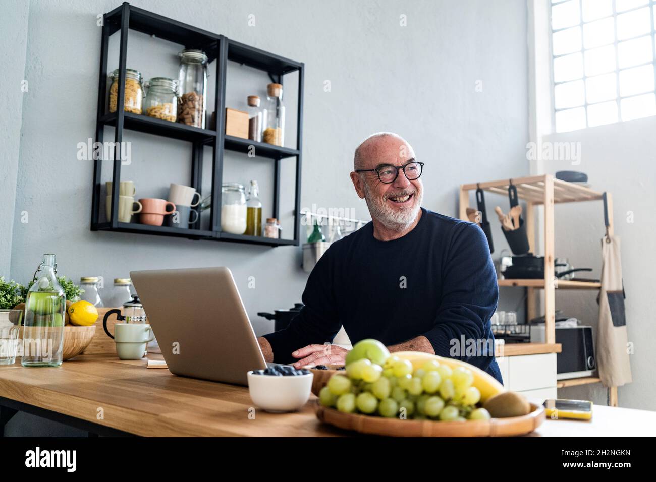 Happy senior man using laptop at kitchen counter Stock Photo