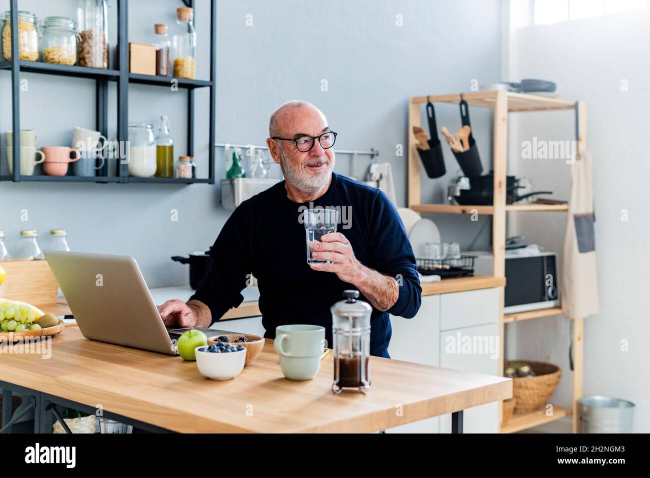 Smiling senior man using laptop at kitchen counter Stock Photo