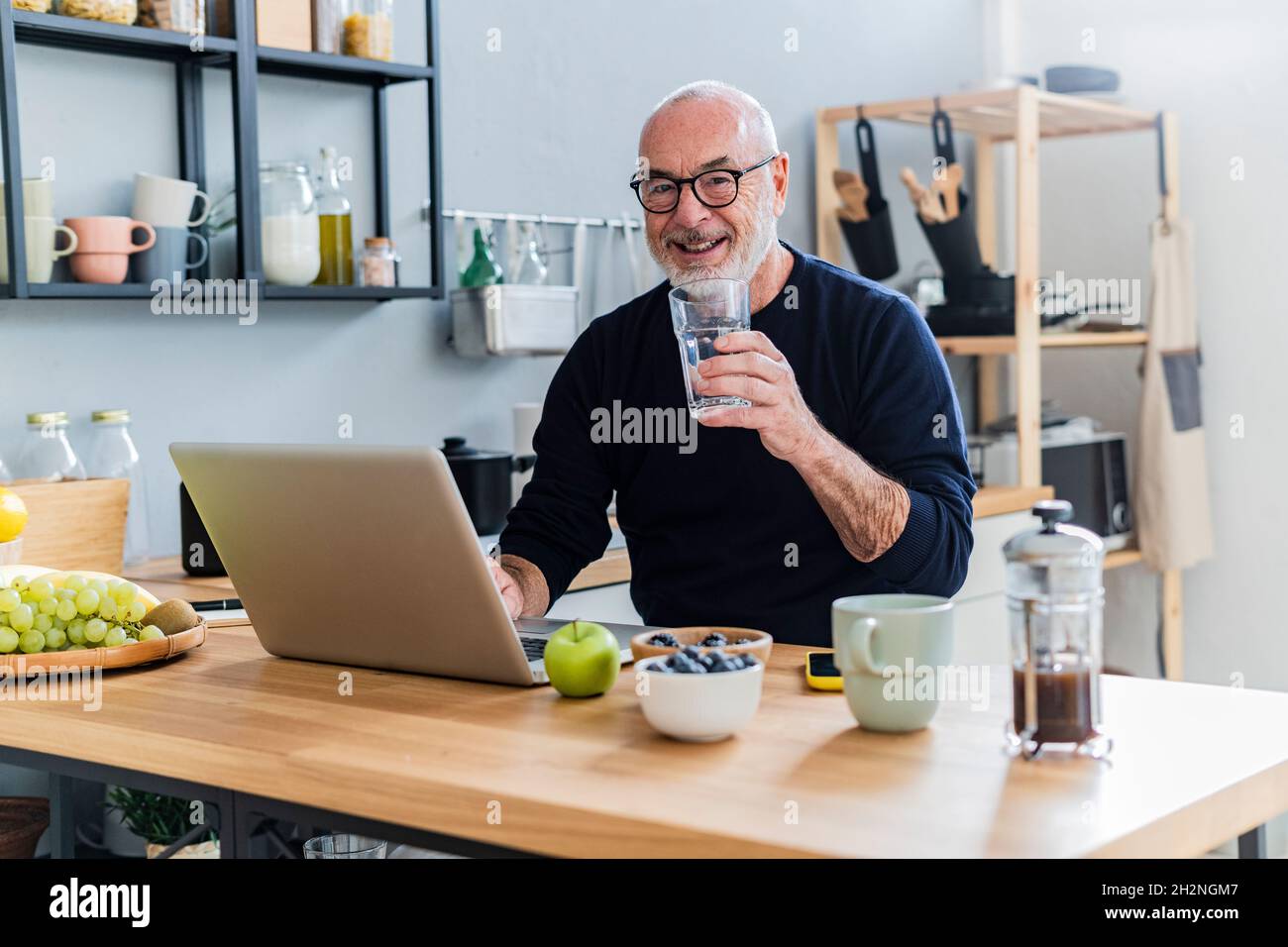 Senior man drinking water while using laptop at home Stock Photo