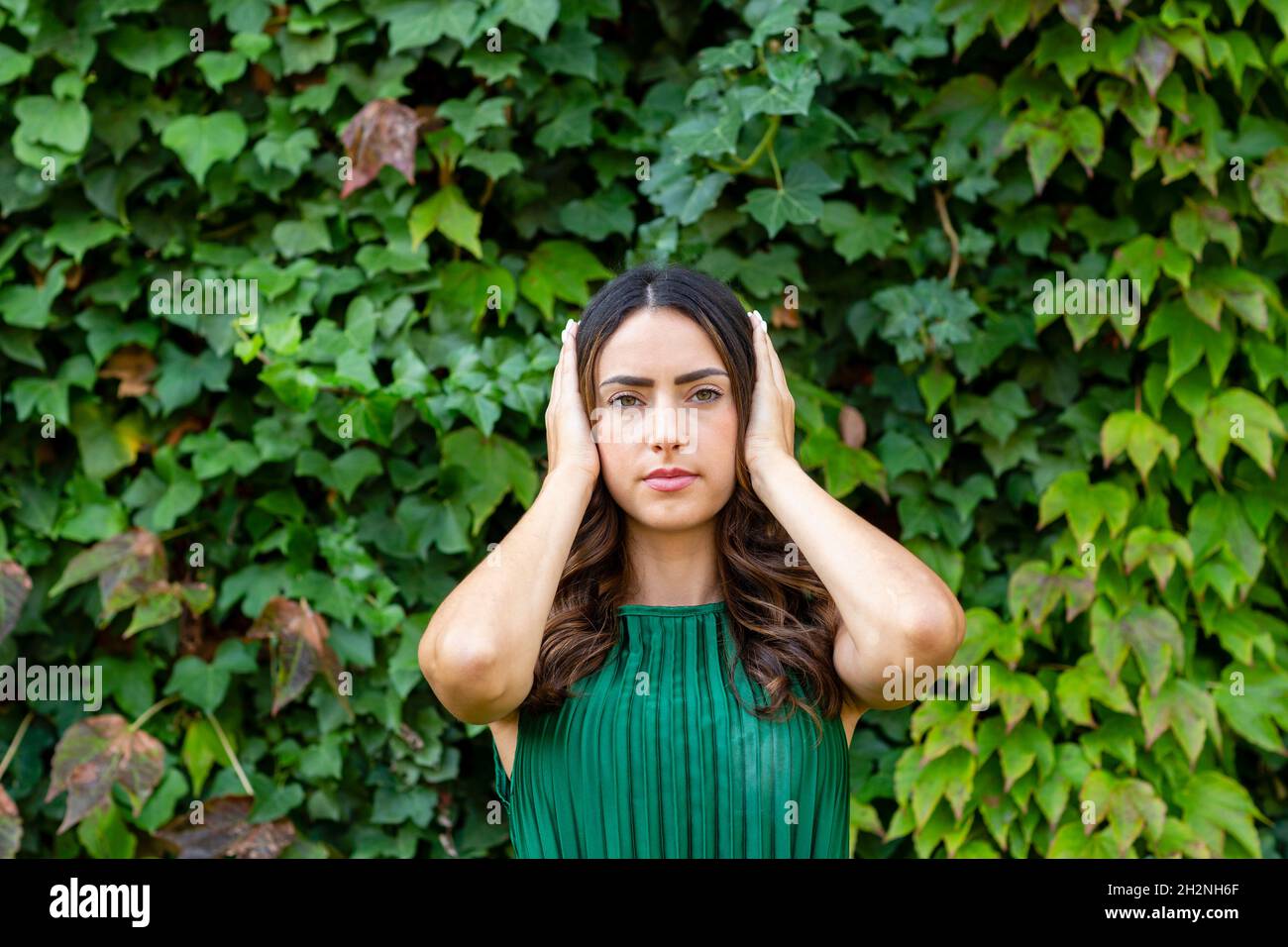 Beautiful woman covering ears with hands in front of green ivy plants Stock Photo