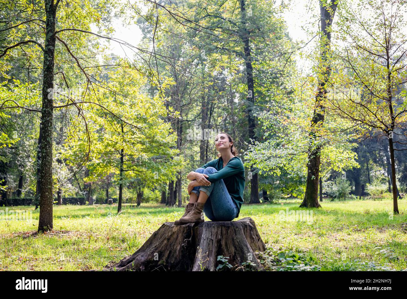 Thoughtful woman sitting in fetal position on tree stump Stock Photo