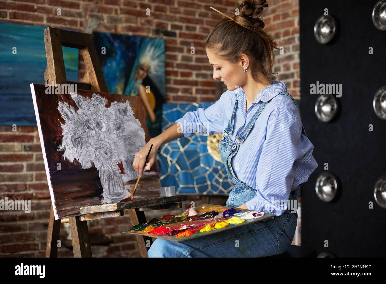 Young beautiful female artist painting still life with sunflower on ...