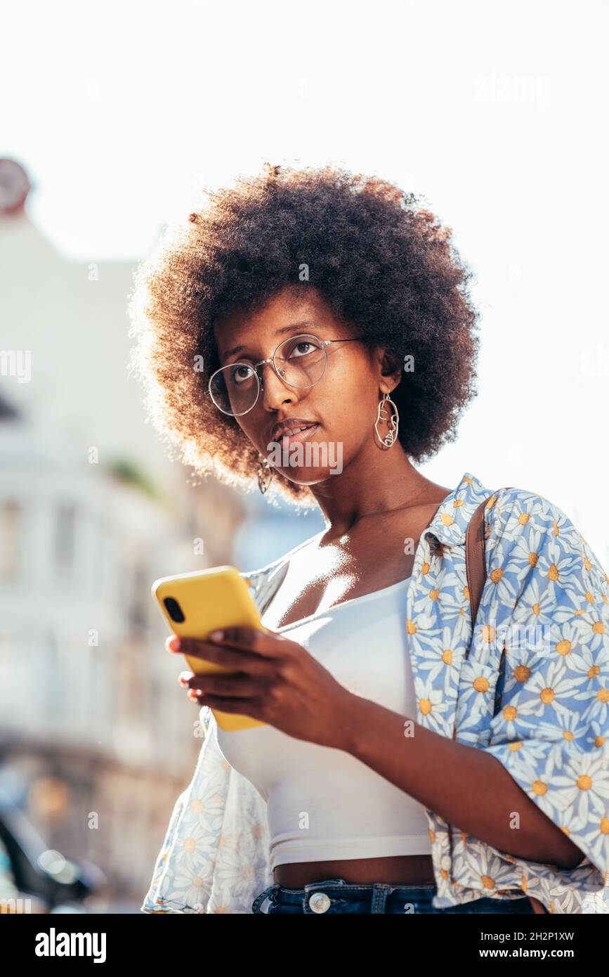 stylish african woman holding her telehone on the streets. She wears trendy casual summer clothing and has afro hairstyle Stock Photo