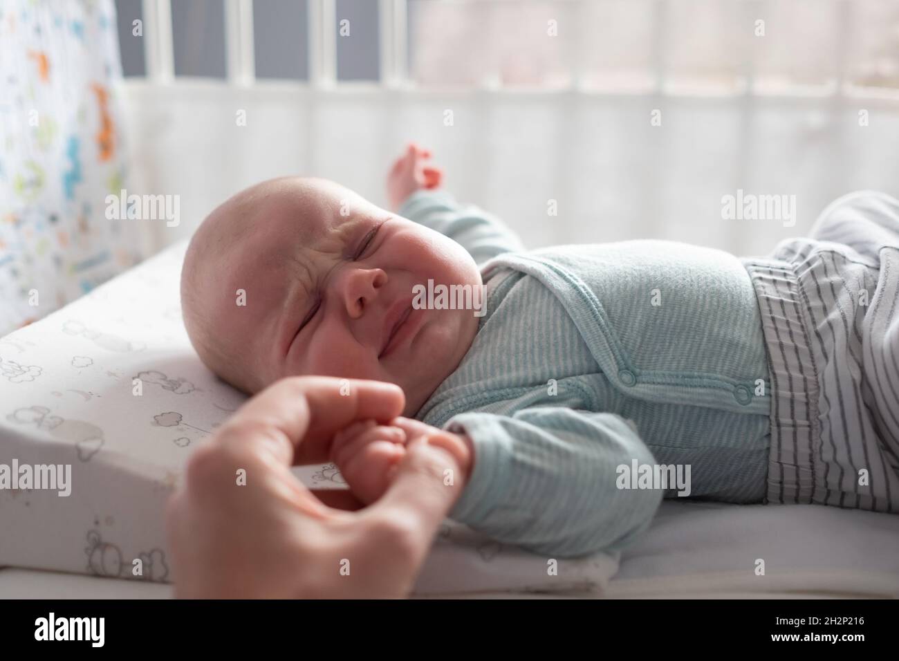 Crying caucasian baby on a bed suffering from colic pain. Stock Photo