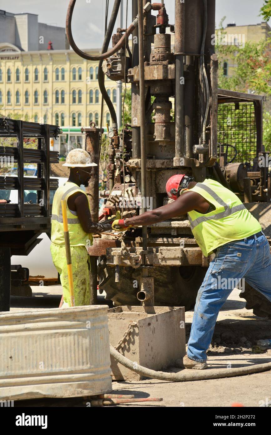 Two African-American construction workers safely drilling hole in city center, adjacent to Wisconsin River, urban renewal, Milwaukee, Wisconsin, USA. Stock Photo