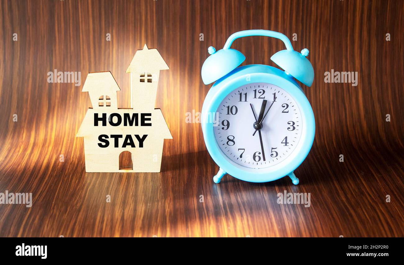 Stay at home, work at home. Coronavirus quarantine concept. House with text and clock on a wooden background. Stock Photo