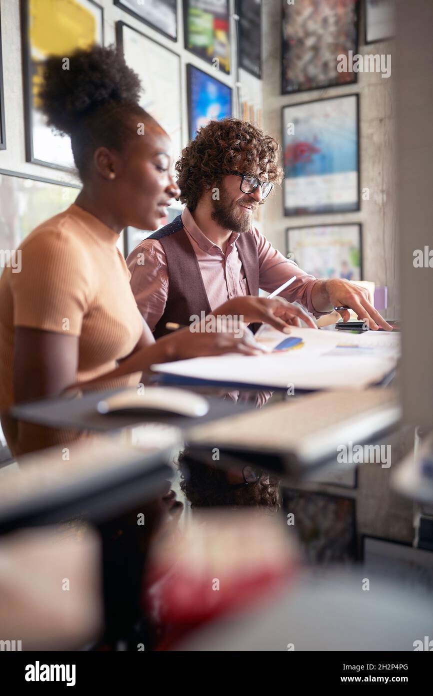 selective focus on a beardy guy working together with his afro american young female colleague, sitting together at the office Stock Photo