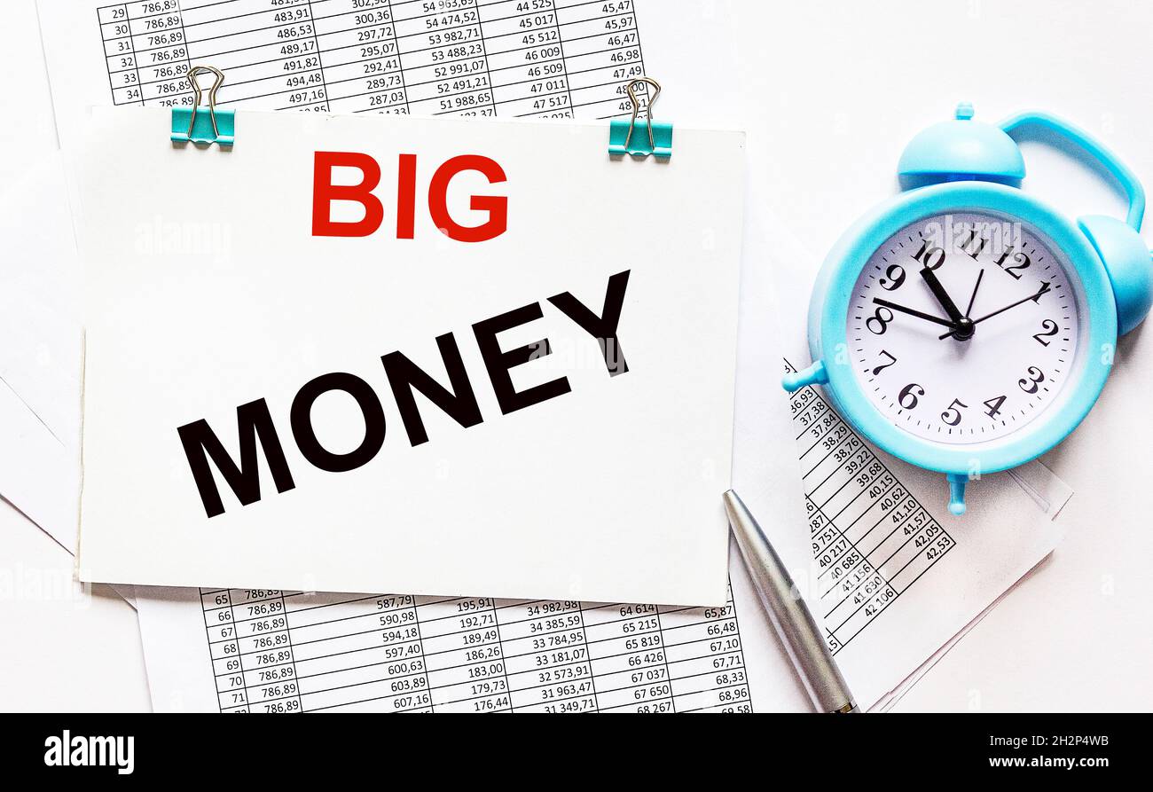 The text Big Money is written on a note that lies on the accounting documents and a white background. Nearby a pen and an alarm clock Stock Photo