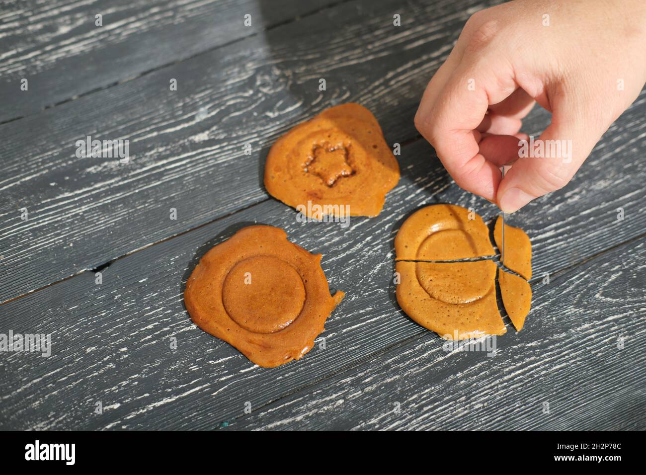 hand breaking dalgona candy Squid game ppopgi, Korean sweets with stamps in the center. Viral trend on cocial media Stock Photo