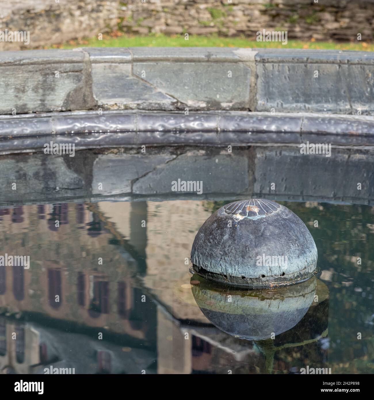 Reflection of Abbey of Ste Foy in basin of cloister fountain, Conques, Aveyron, France Stock Photo