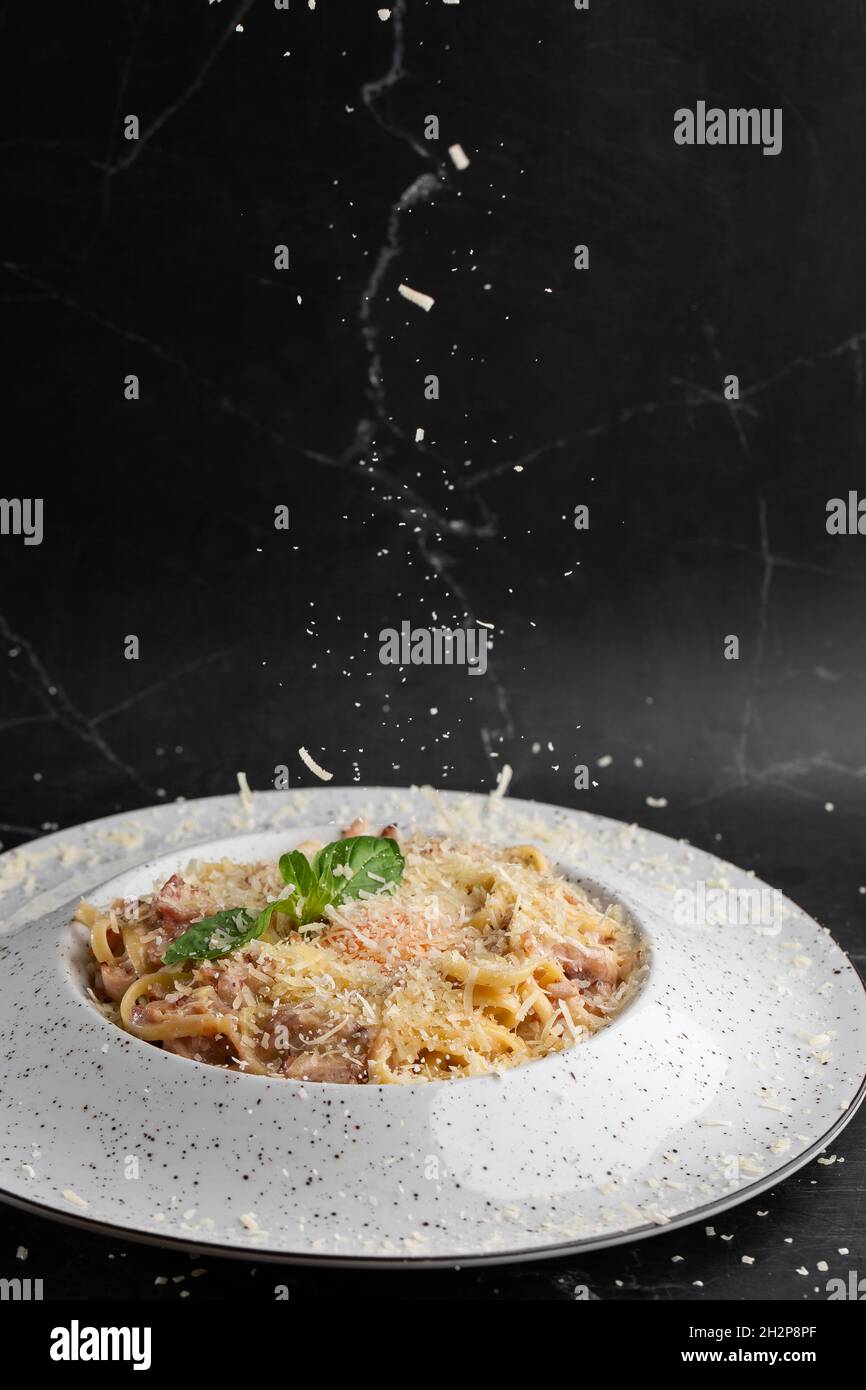 Cheese falling on pasta. Spaghetti with bacon, parmesan, cream sauce and egg yolk on black