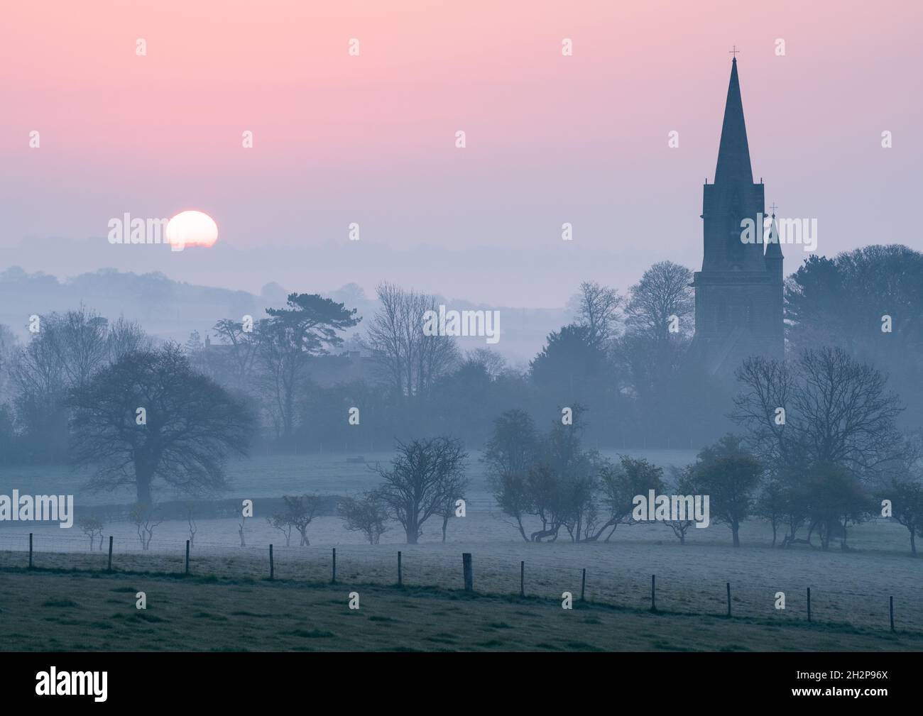 St Barnabas Church in Weeton is prominent amongst hazy layers in the landscape on a spring morning as the sun begins to rise over the horizon. Stock Photo