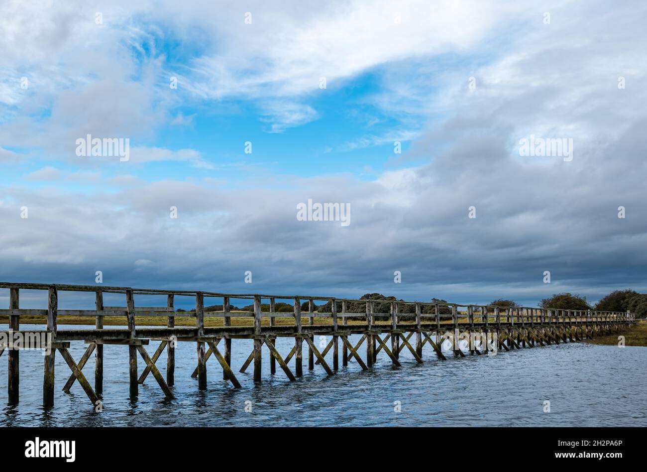 Wooden footbridge over estuary to Aberlady nature reserve with flock of geese in the sky, East Lothian, Scotland, UK Stock Photo