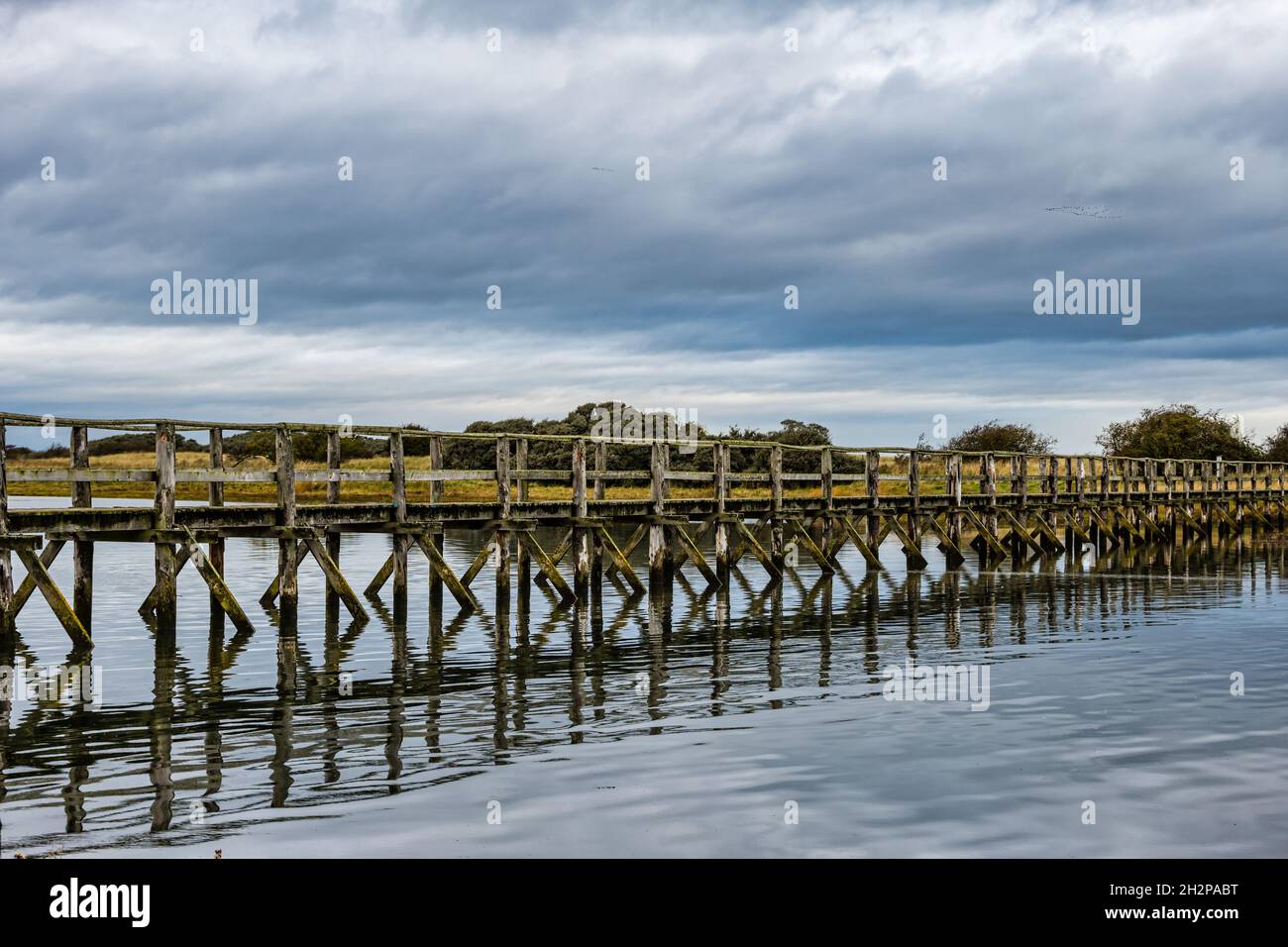 Wooden footbridge over estuary to Aberlady nature reserve with a moody sky, East Lothian, Scotland, UK Stock Photo