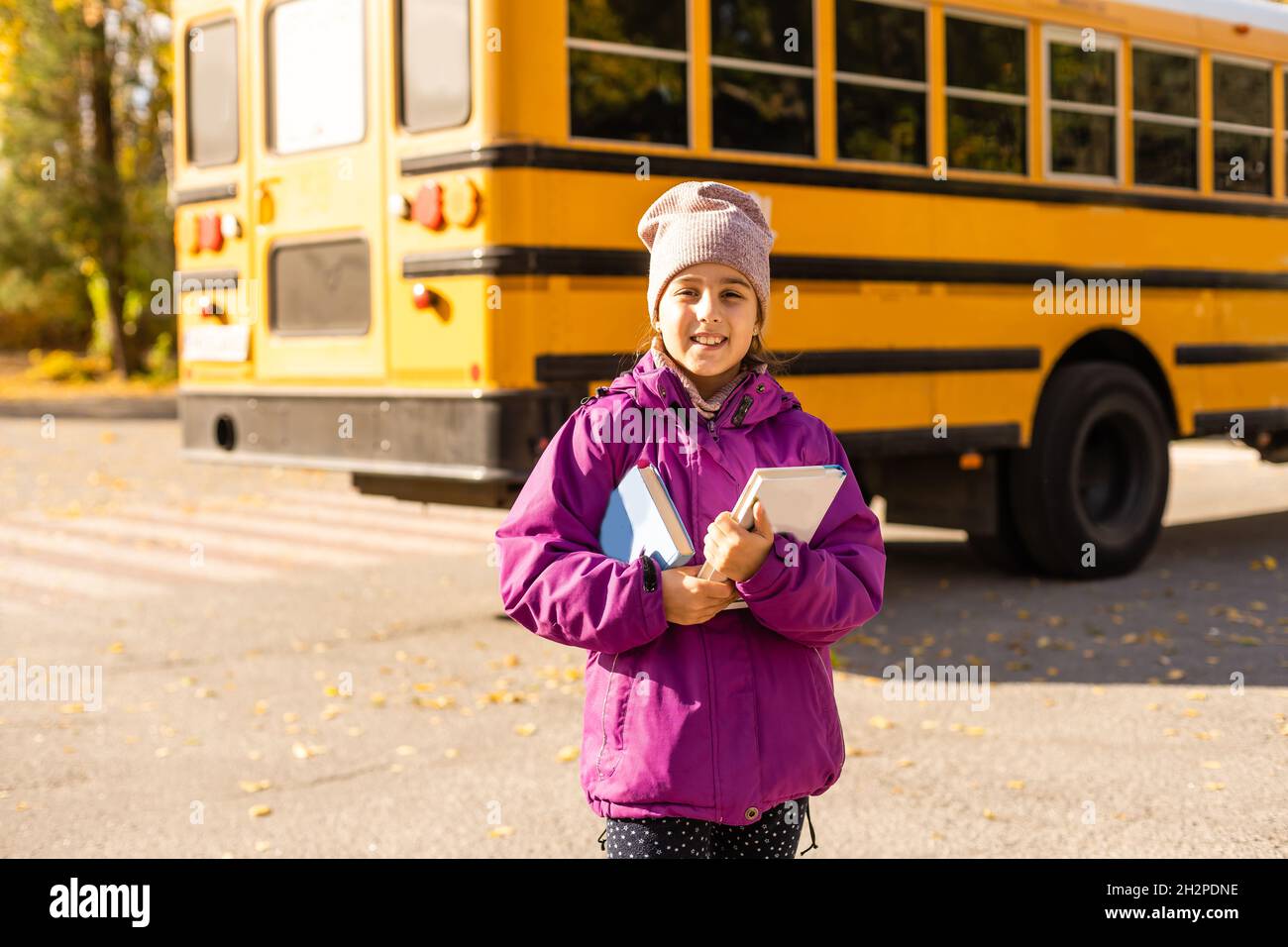 Little girl standing by a big school bus with her books. Stock Photo