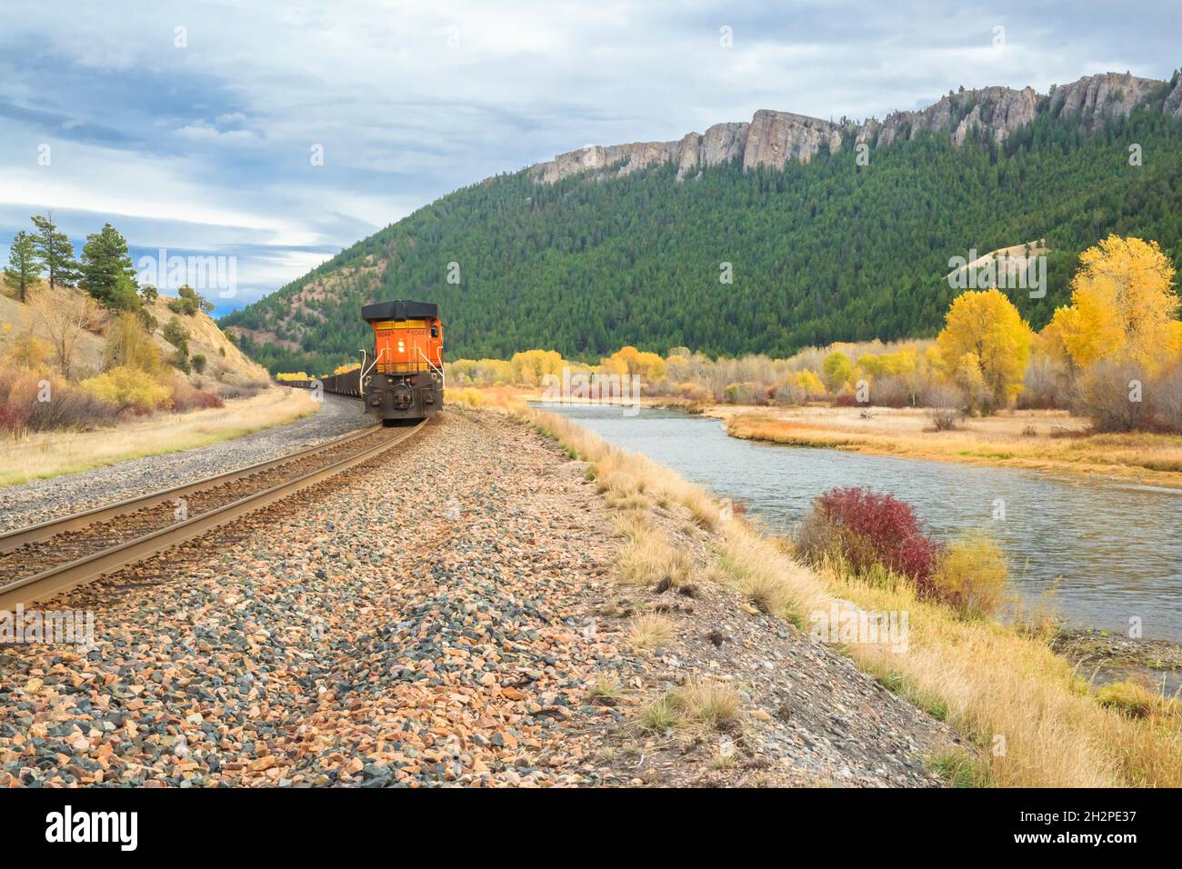 train traveling past cliffs and fall colors along the clark fork river near drummond, montana Stock Photo