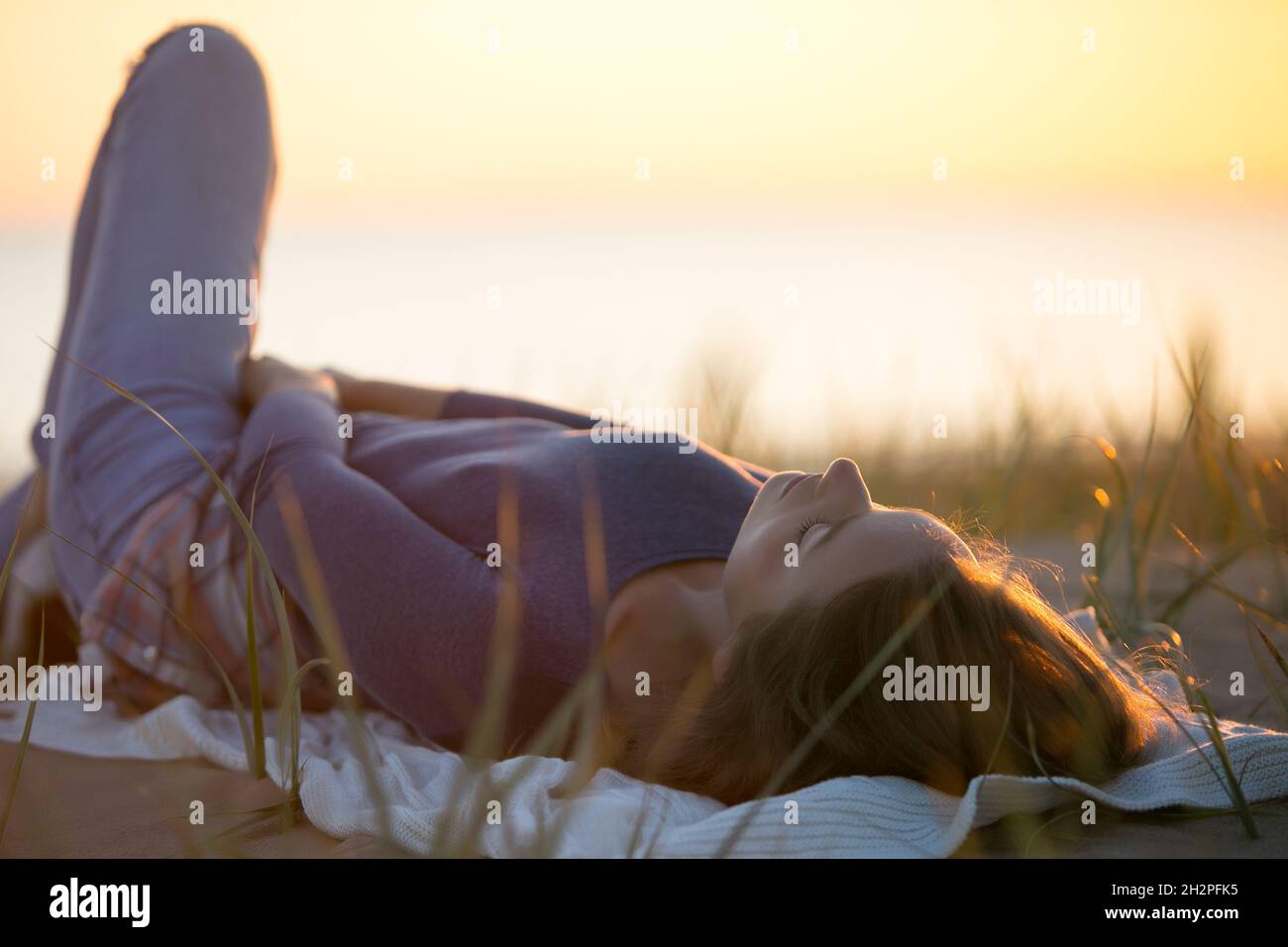 Calm young woman lying on blanket relaxed enjoy autumn sunset in fall field look at setting sun sky Stock Photo