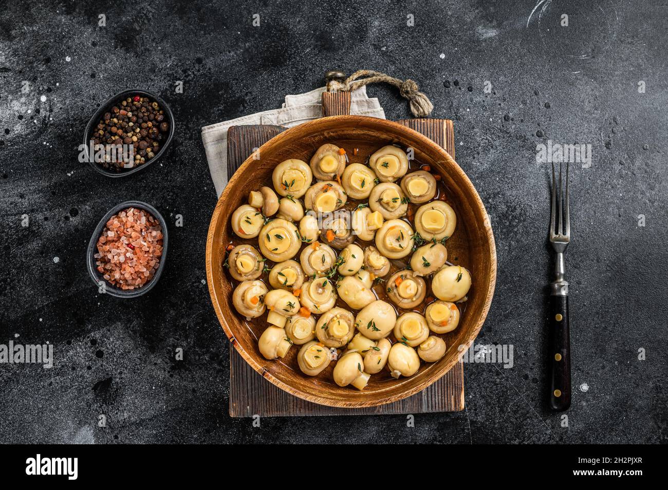Pickled Marinated mushrooms champignons in a wooden plate. Black