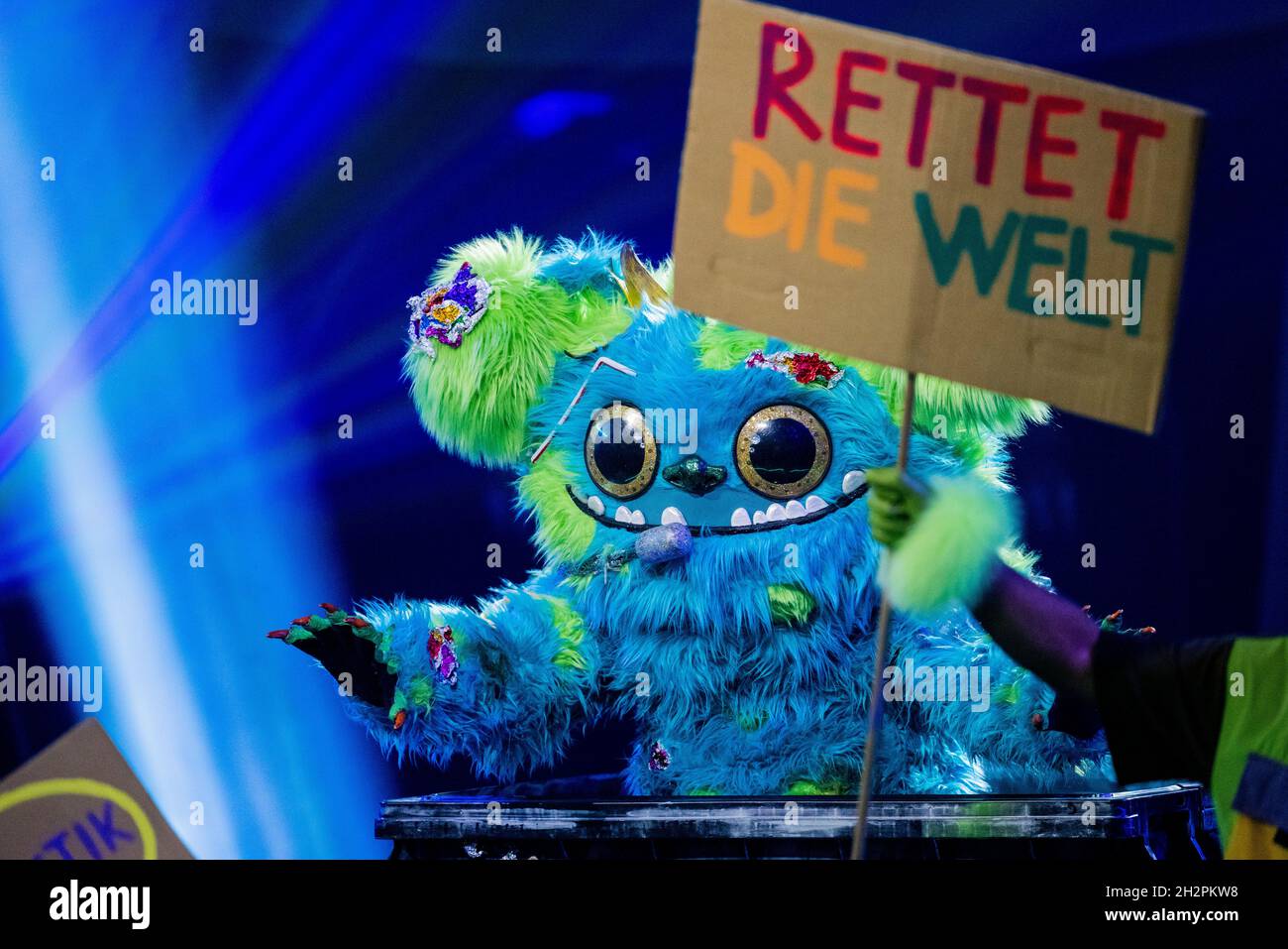 Cologne, Germany. 23rd Oct, 2021. The character 'Mülli Müller' stands on stage in the Prosieben show 'The Masked Singer' and holds a sign with the inscription 'Save the world'. Credit: Rolf Vennenbernd/dpa/Alamy Live News Stock Photo