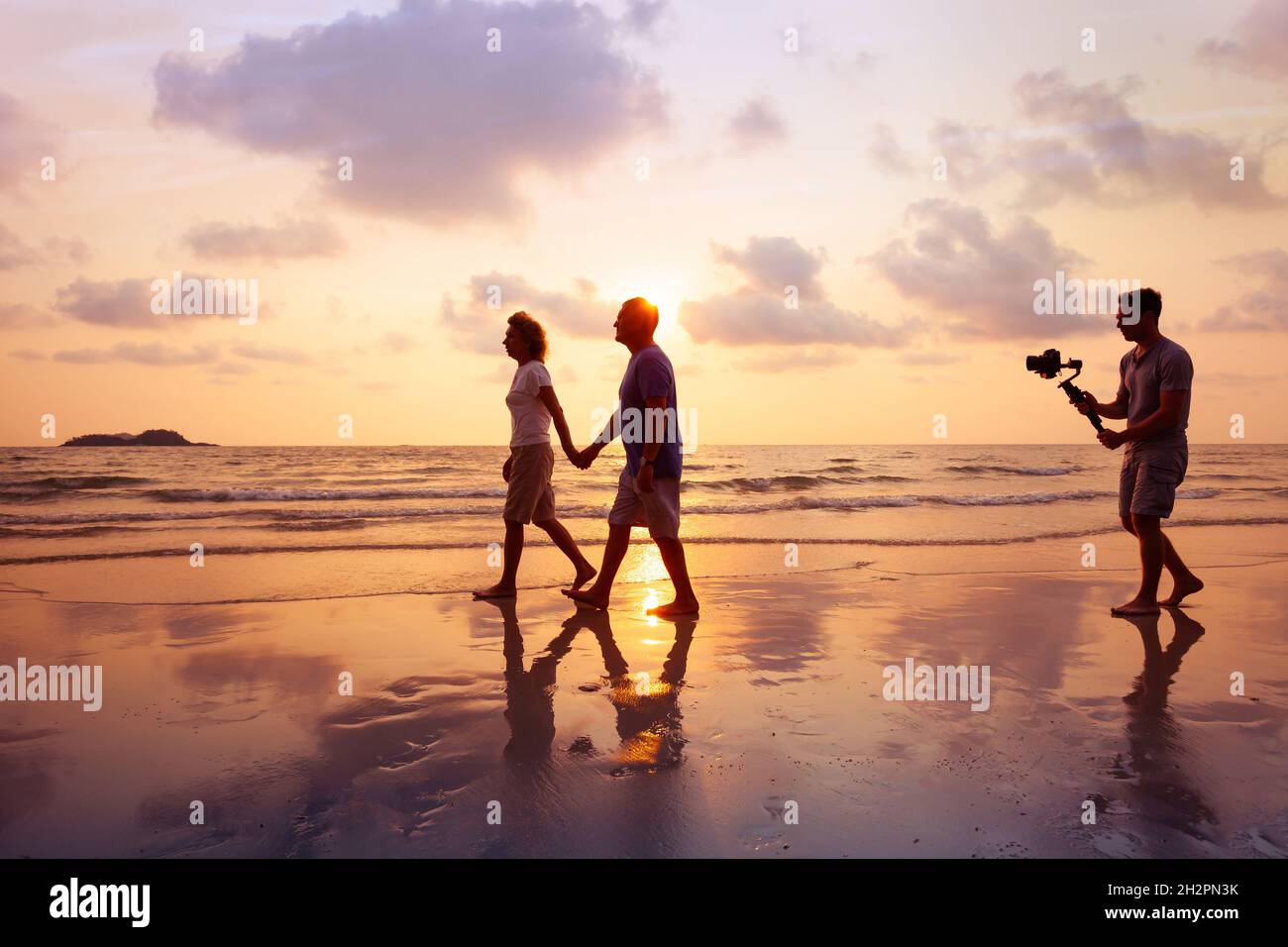 filmmaker filming video of couple with camera stabilizer on the beach at sunset, professional videographer working on film Stock Photo