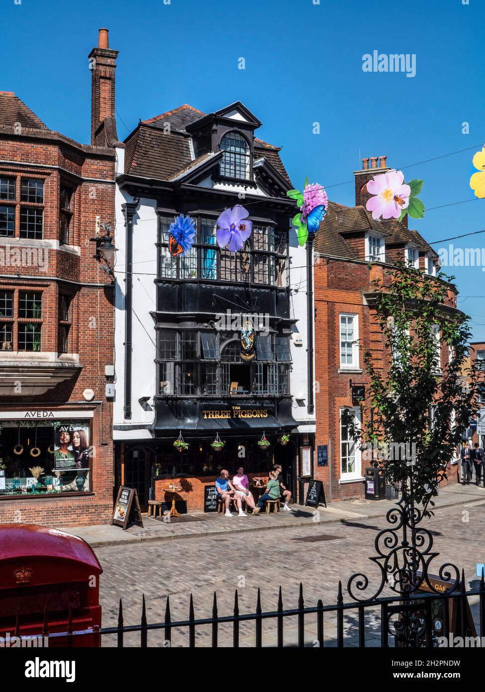 Guildford High Street with colourful autumn illustration banners, traditional red telephone box and historical Three Pidgeons public house behind with alfresco drinkers Guildford Surrey UK Stock Photo