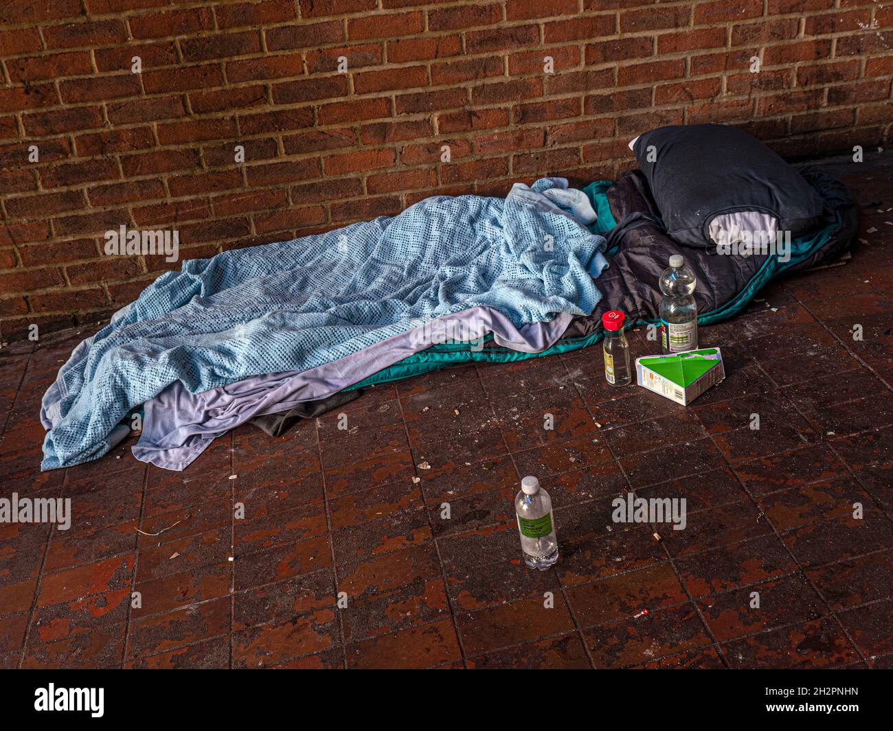 Homeless persons bed still life, in the vestibule entrance to a Guildford Surrey UK Car Park. Poignant reminder of life on the street for the less fortunate, with water bottles and a sandwich carton for sustenance. Stock Photo