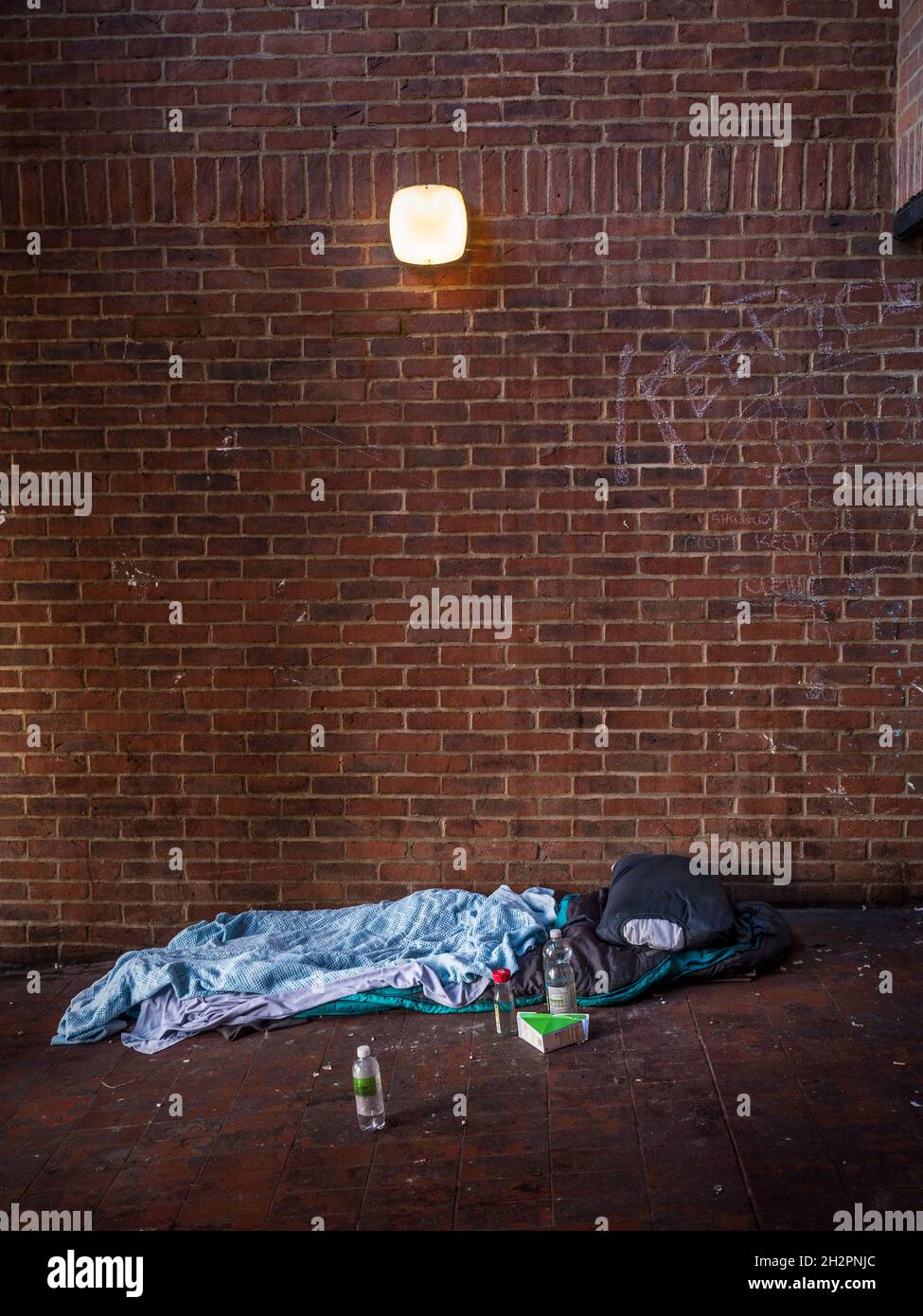 Homeless persons bed in still life, in the vestibule entrance to a Guildford Surrey UK Car Park. Poignant grim and stark reminder of life on the street for the less fortunate, with water bottles and a sandwich carton for sustenance. Stock Photo